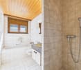 White tiled walls, white tiled floor, wooden ceiling, bathtub, sink, shower head, toilet, towel racks