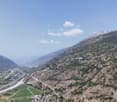Mountain valley with river, surrounded by mountains, green fields, small settlement, clear sky, scattered clouds