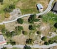 Wide lot with multiple buildings and a winding driveway, surrounded by greenery and trees. The terrain is uneven with some rocky sections.