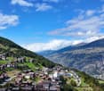 Town on a mountainside, surrounded by lush green meadows, mountains, a clear blue sky with scattered clouds