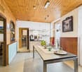 open space with dining table, kitchen area, wooden wall paneling, wooden floor, shelves, hanging lamps, framed picture, large windows