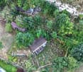 Overgrown land, several dilapidated houses, electrical poles and wires, large stone wall, surrounded by green vegetation