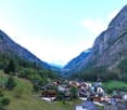small village nestled in a valley, surrounded by green meadows, trees, and rocky mountains