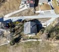 Aerial view of several houses, each with a distinct roof design. Roads leading up to the properties and a car parked near one of the houses. The houses are surrounded by barren fields and sparse vegetation.