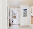 White walls, tile floor, archway leading to terrace, paintings on the wall, small bench