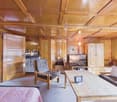 living room with wooden walls, wooden chair, wooden table, TV, couch, wooden cabinet, lamp, carpet, bed