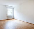 Empty room with wooden floor, white walls, and windows.