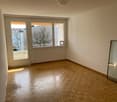 Empty room with wooden parquet flooring, glass doors leading to a balcony, large windows with a tree view outside