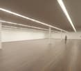 empty room, hardwood floor, long fluorescent ceiling lights, tall white walls, white interior, 2 people