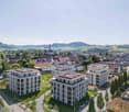 Aerial view of residential buildings with solar panels, modern architecture, rooftop garden, nearby green areas, and a scenic view.