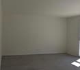 Empty room with white walls, gray concrete floor, and a large window providing natural light.