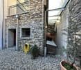 Stone building, raised ground floor, balcony with metal railing, entrance door, potted plants
