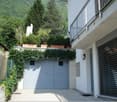 white exterior walls, balcony with railing, double grey garage doors, large potted plants on garage roof, small plants on exterior wall