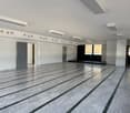 Large open space with gray marble-like flooring, white walls, and recessed lighting fixtures. The space appears to be a commercial or office area, with a door visible in the background.