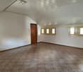 Empty room with wooden door, three windows, white walls, and brown tiled floor.