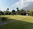 large well-maintained lawn with scattered trees and shrubs, two buildings on the sides, mountains in the distance