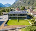 Modern house with solar panels on the roof, glass facade, surrounded by greenery, mountains in the background