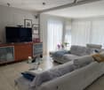 modern living room with white leather couches, glass coffee table, flat screen TV, wooden entertainment center, white curtains