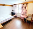 single bed, bedside table, TV, table, chair, window with curtains