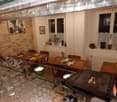 wooden dining tables, chairs, wine glasses, bar with wine bottles, framed pictures on the wall, small plants on the window sill