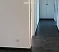 Corridor with a white wall, gray floor, white cabinet with two doors, and a power outlet.