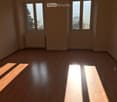 empty room with wooden floor, two large windows, white walls, radiator, sun coming in