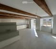 empty room with white kitchen, wooden beams, fireplace, tile flooring