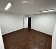 Empty room with white walls, wooden floor, ceiling lights, open door leading to another room