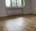 Empty room with hardwood floors, windows with open casement windows, white walls, radiator.