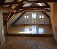 Wooden beams ceiling, white painted walls, wooden floor, three windows, small door