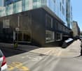 Modern building with glass windows, black exterior, located on a street with parked cars