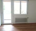 empty room with wooden floor, sliding glass door, windows, radiator, white walls