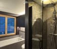 Bathroom with shower, bathtub, sink, glass shower door, dark tiled walls, wooden window, toilet