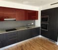 Modern kitchen with dark wood cabinets, red upper cabinets, gray tile backsplash, granite countertops, and built-in appliances including a dishwasher