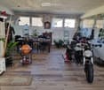 large room, wooden floor, dining table with chairs, motorcycles, plants, paintings on wall