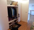 walk-in closet with white shelves, hangers, storage boxes, basket, shoes on the floor, and a black door