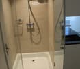 Bathroom with walk-in shower, tile walls, open door, small basin area