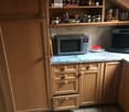 light wood cabinets, tiled backsplash, countertop, microwave, plate with red lid, outlet, open drawer