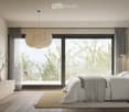 A bedroom with sliding glass doors leading to a balcony, large bed, white bedding, gray curtains, a large window, hanging lamp, wooden bedside table with books, wooden cabinet with books and a plant