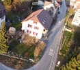 Aerial view of the building, located on the corner of the street, surrounded by other houses, and green grass, white windows