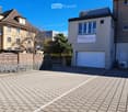 Front parking lot with a brick floor, wooden fence with a gate, white garage with windows, and two other neighboring buildings