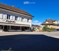 two story commercial building, storefronts with awnings, street with a car parked on the side, another house in the background, sunny weather