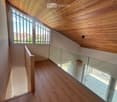 Spacious hallway with wooden flooring and ceiling, large windows, glass railing leading to a balcony area.