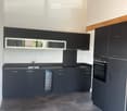 Modern kitchen with dark grey cabinets, stainless steel sink, and built-in oven. Features a sleek design with a wooden slanted ceiling and large windows.