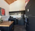 modern kitchen with wooden ceiling, black cabinets, wooden countertop, island, wine cooler, oven, sink, coffee machine, flowers, painting