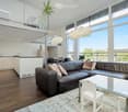 Open plan living space with living room and kitchen, large windows, balcony, and ceiling lamps