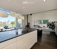 modern kitchen with large black countertops, white cabinets, chandeliers, balcony with outside view, large windows
