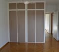 Empty room with large built-in wardrobes, parquet floor, white walls