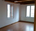 Empty room with wooden floor, two windows, white walls, wooden ceiling, and a white heater.