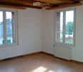 an empty room with wooden floors, white walls, two large windows, a white radiator under the right window, and a wooden ceiling with exposed beams
